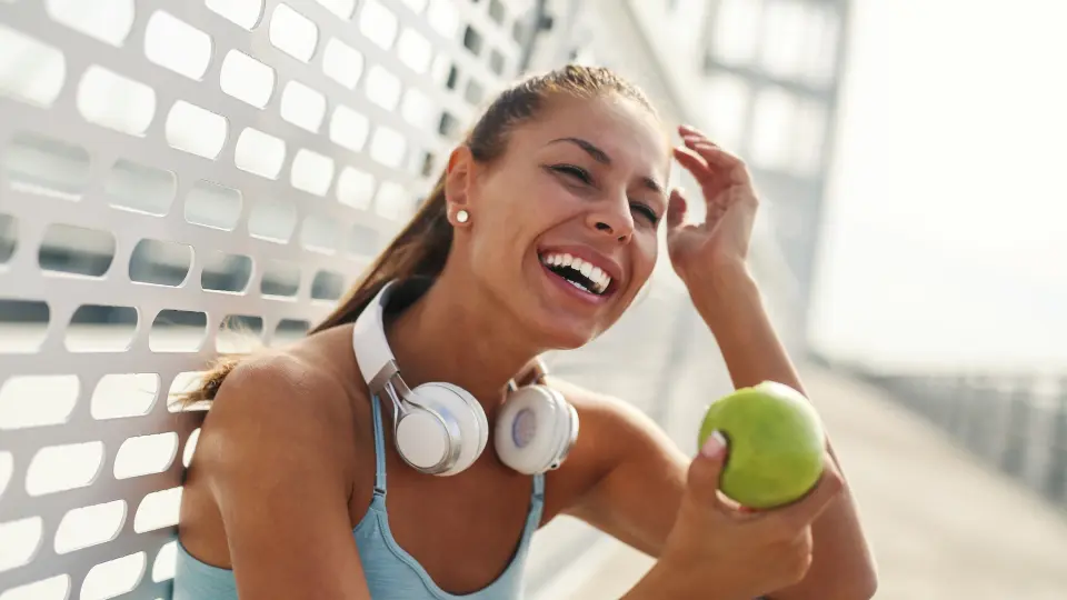 A woman wearing headphones and holding an apple in her hand.