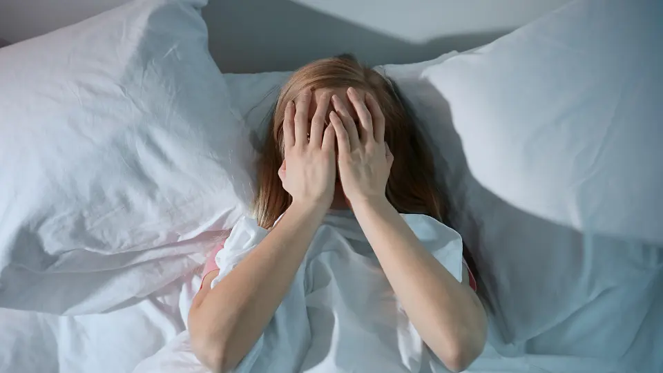 A woman lying in bed, covered in white sheets, peacefully resting.