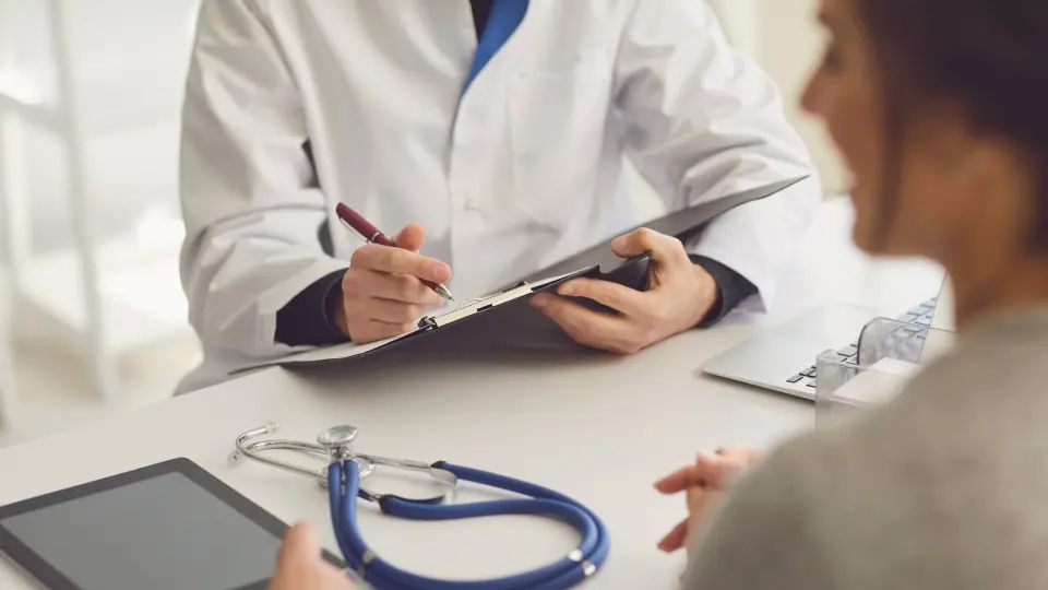 A doctor writing on a clipboard as a patient observes.