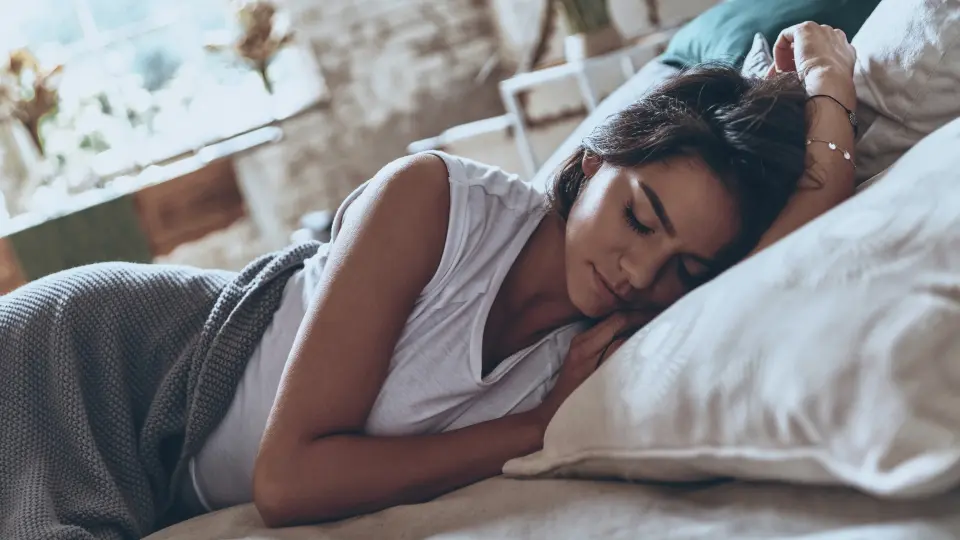 A woman peacefully sleeping on a bed with fluffy pillows.