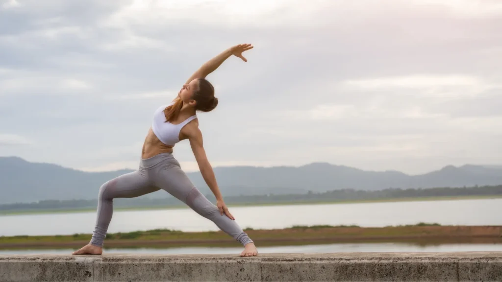 A woman gracefully performing a yoga pose on a concrete wall, showcasing strength and balance.