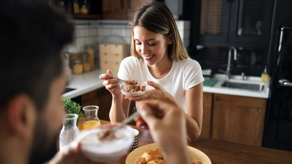 A couple enjoying breakfast together in their kitchen, with the man and woman sitting at the table and eating.