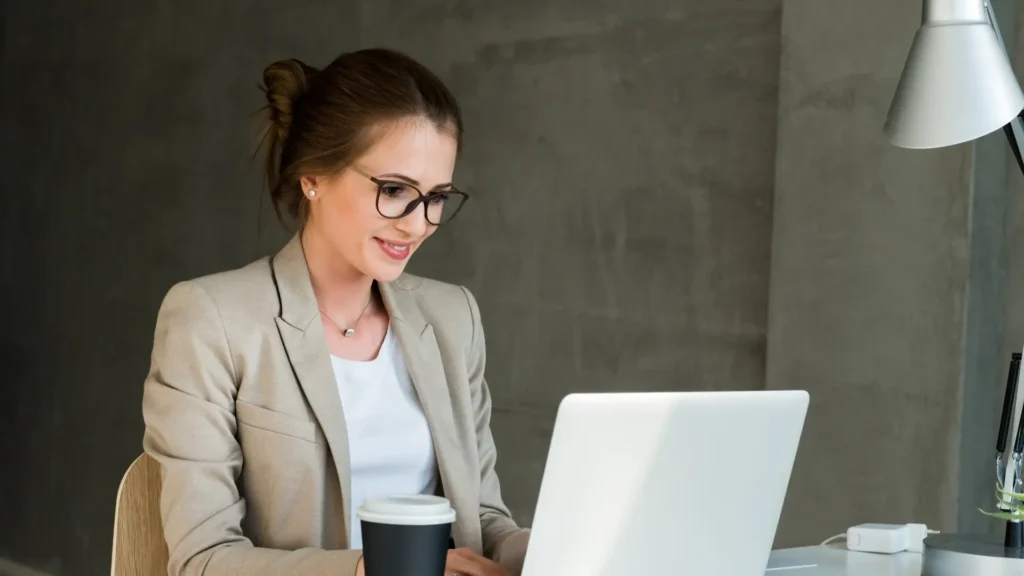 A woman wearing glasses focused on her laptop, working diligently.