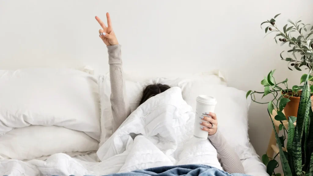 A woman lying in bed with her hands raised, possibly stretching or waking up.