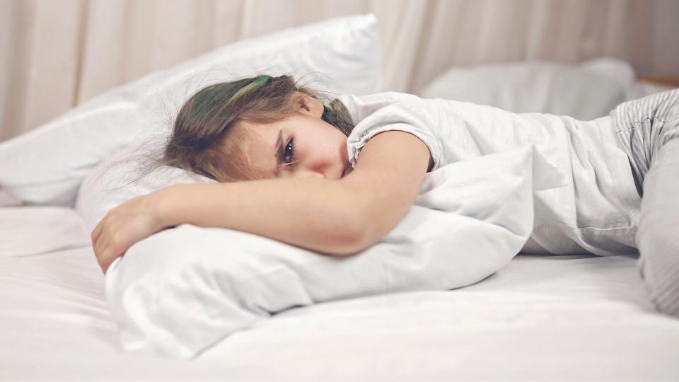 A young girl enjoying a cozy moment on a bed surrounded by fluffy pillows.