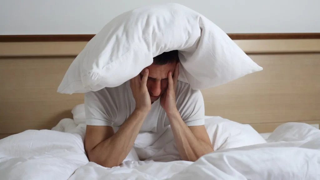 A man laying in bed with a pillow covering his head. PTSD Sleep Apnea