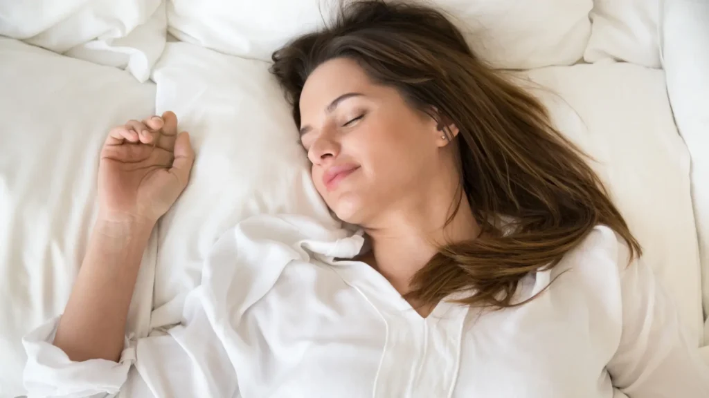 A woman peacefully sleeping on a white bed, enjoying a restful slumber.