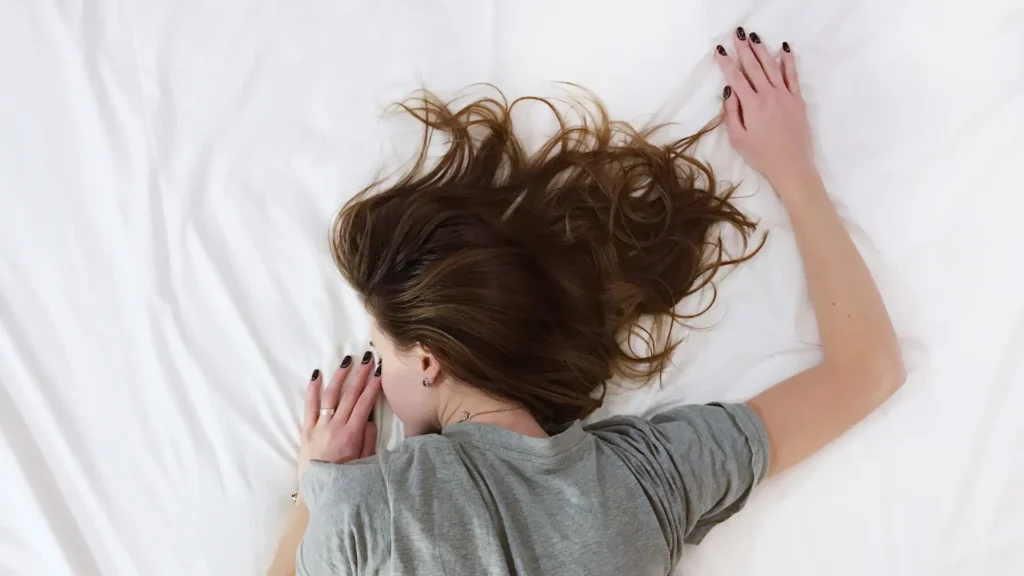 A woman laying on a bed with her hair blowing in the wind.