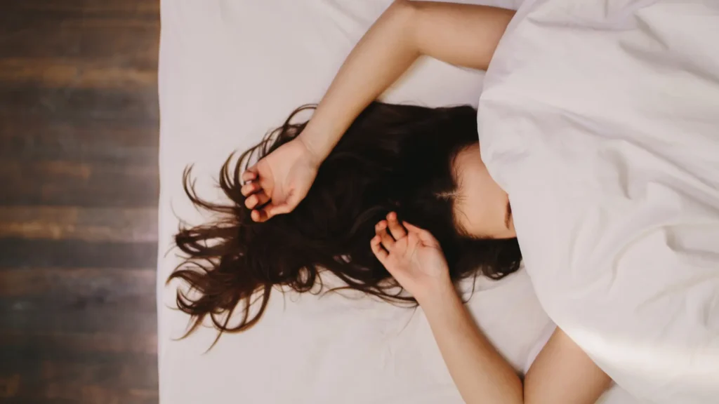 A woman laying in bed with her head under a white sheet, peacefully resting.