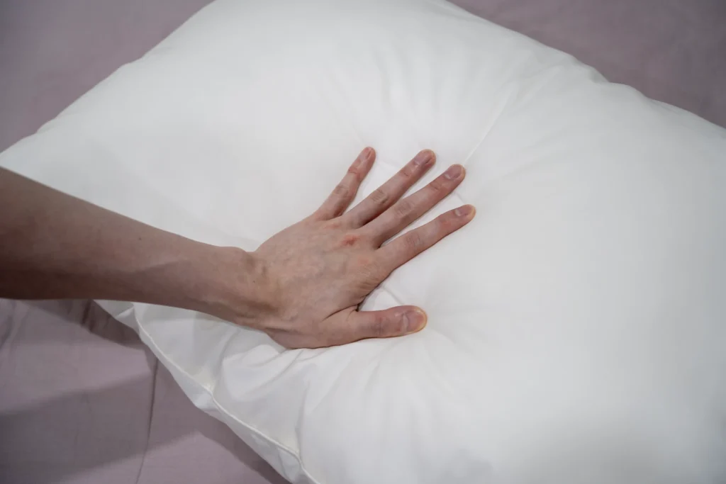 A hand pressing down on a Simmons DeepSleep pillow, demonstrating its softness and plush cushioning for optimal comfort.